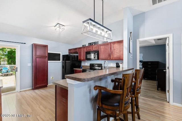 kitchen with reddish brown cabinets, light wood-type flooring, black appliances, a peninsula, and lofted ceiling