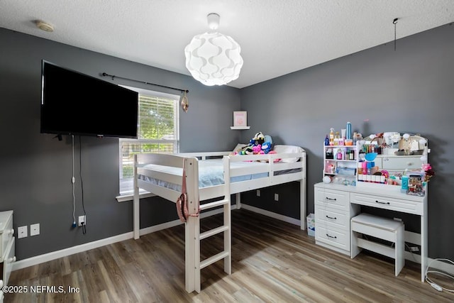bedroom featuring baseboards, a textured ceiling, and light wood finished floors