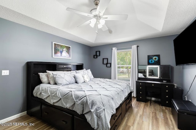 bedroom featuring a ceiling fan, a tray ceiling, baseboards, and light wood-type flooring