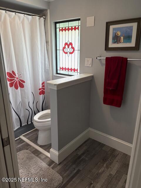 bathroom featuring toilet, baseboards, curtained shower, and wood finished floors