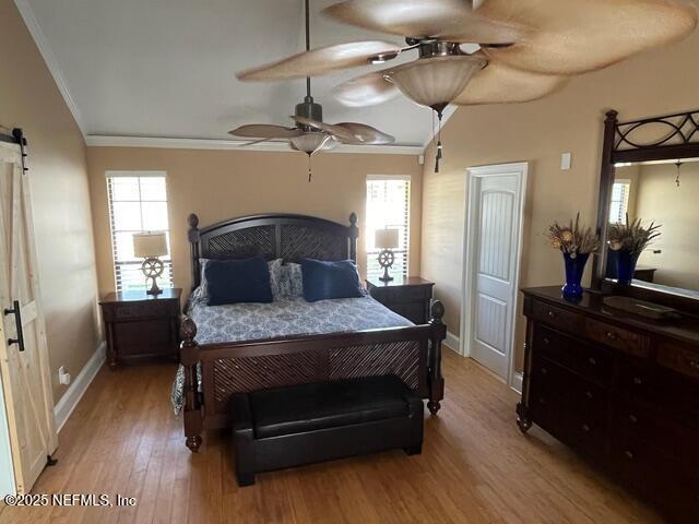 bedroom featuring crown molding, baseboards, light wood finished floors, and a barn door
