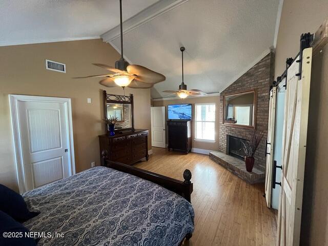 bedroom featuring a barn door, a fireplace, vaulted ceiling with beams, wood finished floors, and visible vents