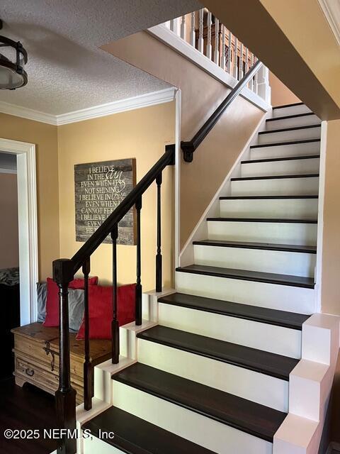 stairway with a textured ceiling, ornamental molding, and wood finished floors