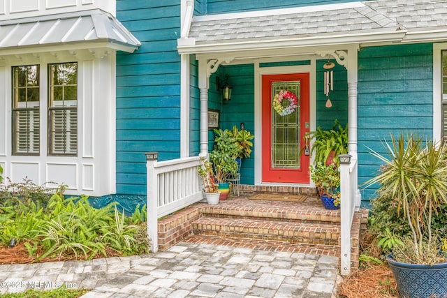 view of exterior entry with roof with shingles