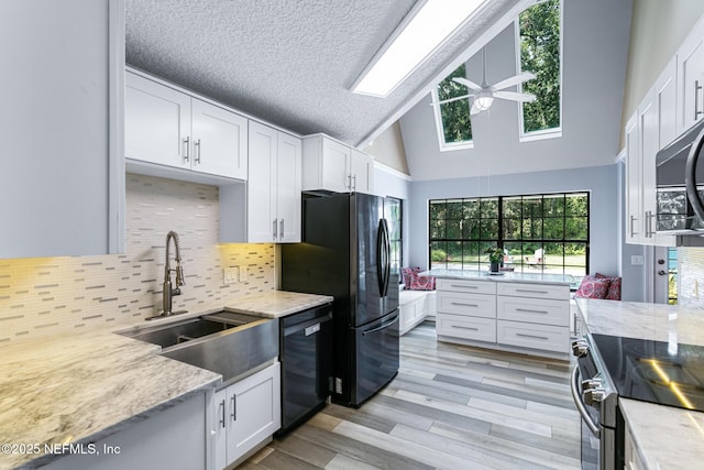 kitchen with a sink, white cabinets, black appliances, and high vaulted ceiling