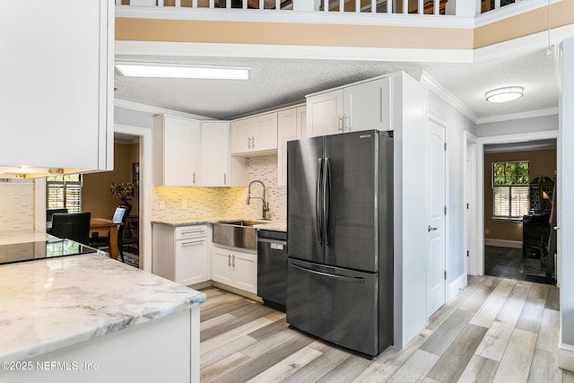 kitchen with freestanding refrigerator, ornamental molding, black dishwasher, white cabinetry, and a sink