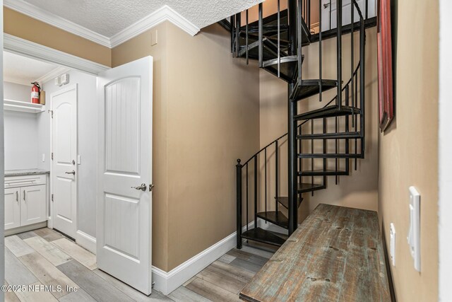 staircase with crown molding, baseboards, a textured ceiling, and wood finished floors