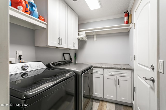 washroom featuring cabinet space, a textured ceiling, light wood-style flooring, ornamental molding, and washer and clothes dryer
