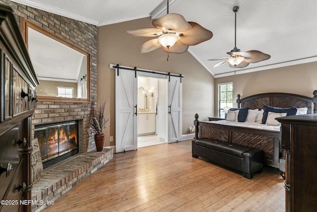 bedroom featuring ornamental molding, a fireplace, baseboards, a barn door, and light wood-style flooring