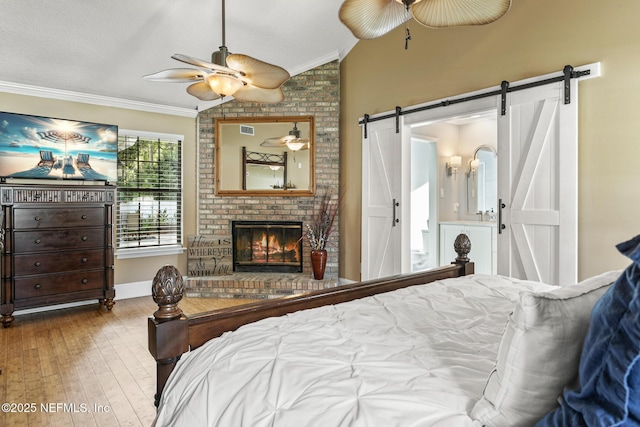 bedroom featuring crown molding, a fireplace, vaulted ceiling, a barn door, and wood-type flooring