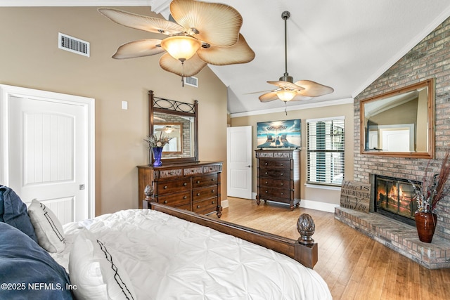 bedroom featuring visible vents, ornamental molding, wood-type flooring, a fireplace, and vaulted ceiling