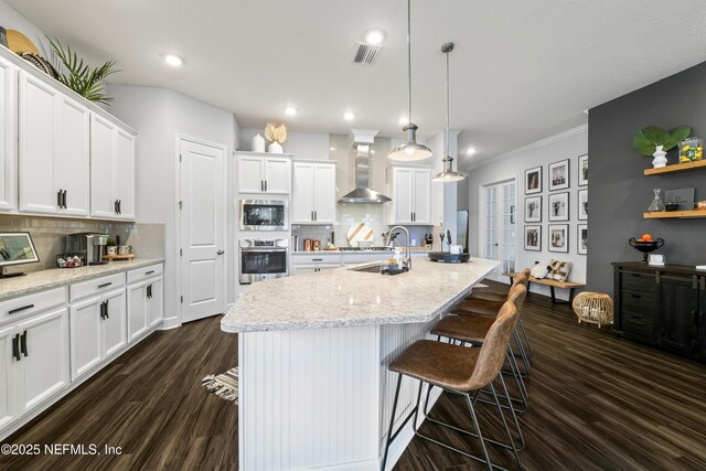 kitchen with wall chimney range hood, stainless steel appliances, dark wood-type flooring, white cabinets, and ornamental molding
