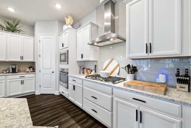kitchen with wall chimney exhaust hood, appliances with stainless steel finishes, white cabinetry, backsplash, and dark wood-type flooring