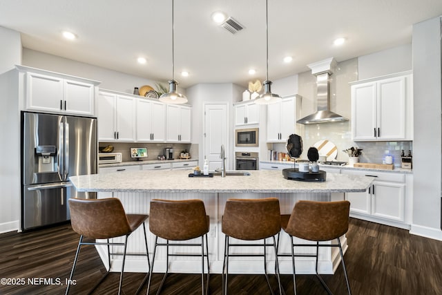 kitchen with appliances with stainless steel finishes, a sink, wall chimney range hood, white cabinets, and recessed lighting