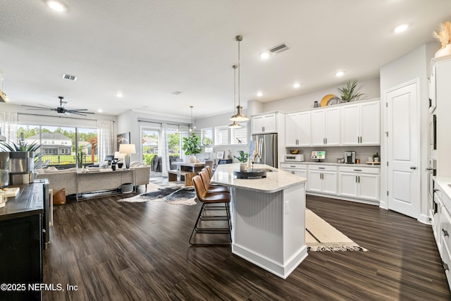kitchen featuring appliances with stainless steel finishes, dark wood finished floors, open floor plan, a center island with sink, and white cabinetry