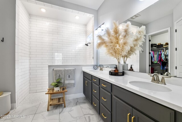full bath featuring walk in shower, double vanity, marble look tiles, and a walk in closet