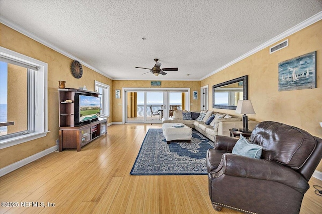 living area with light wood-type flooring, ornamental molding, ceiling fan, a textured ceiling, and baseboards