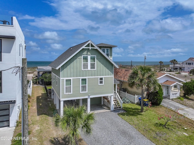raised beach house featuring fence, board and batten siding, a water view, a carport, and gravel driveway