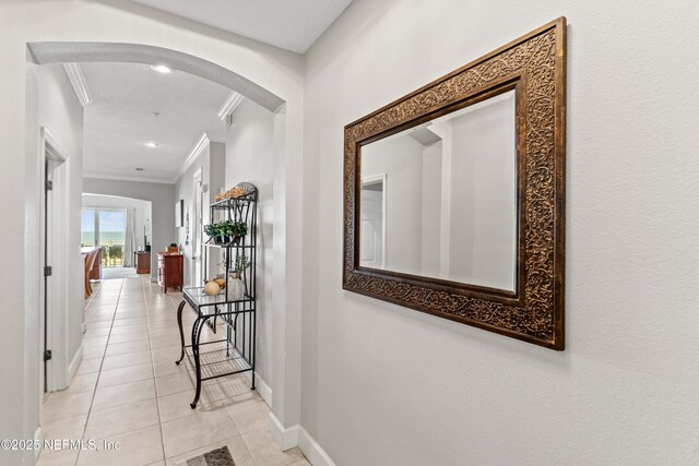 hall with crown molding, light tile patterned floors, arched walkways, baseboards, and recessed lighting