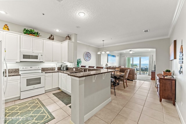 kitchen with white appliances, a peninsula, ornamental molding, light tile patterned flooring, and white cabinets