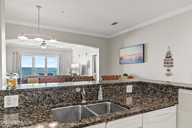 kitchen featuring a sink, ornamental molding, dark stone countertops, white cabinetry, and a ceiling fan