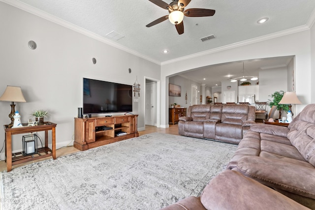 living room with ceiling fan, arched walkways, crown molding, baseboards, and a textured ceiling