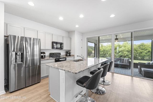 513 Sandstone Dr, Saint Augustine, FL 32086 - kitchen with light stone countertops, a sink, light wood finished floors, a breakfast bar area, and black appliances