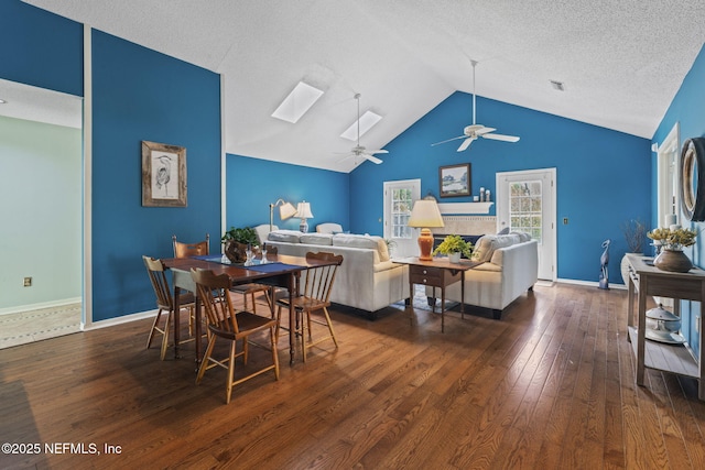dining space featuring ceiling fan, baseboards, vaulted ceiling with skylight, and hardwood / wood-style floors