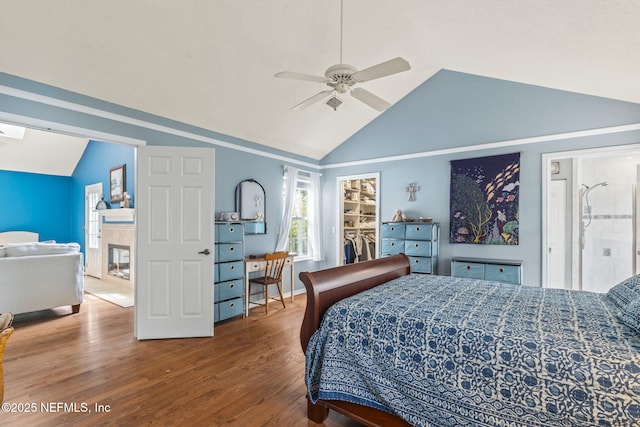 bedroom with a walk in closet, a ceiling fan, a tiled fireplace, wood finished floors, and lofted ceiling