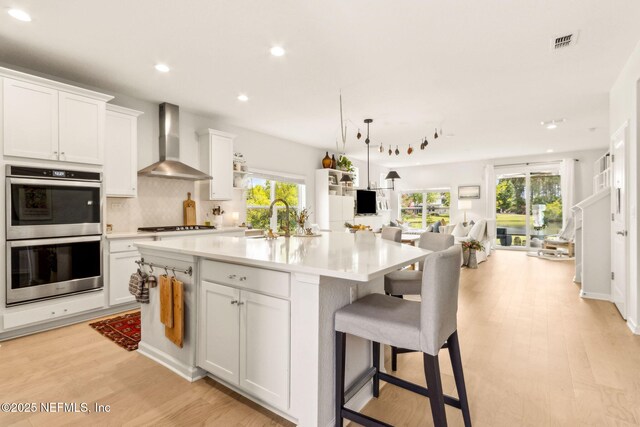 kitchen featuring visible vents, appliances with stainless steel finishes, open floor plan, recessed lighting, and wall chimney exhaust hood