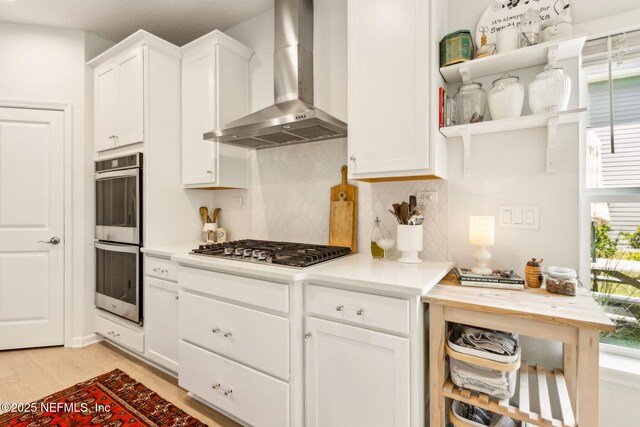kitchen with backsplash, light wood-type flooring, white cabinets, stainless steel appliances, and wall chimney exhaust hood