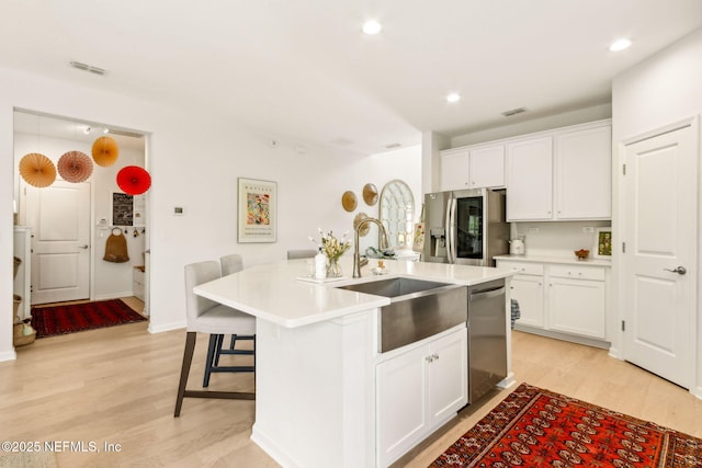 kitchen featuring visible vents, a sink, white cabinets, light wood finished floors, and stainless steel appliances
