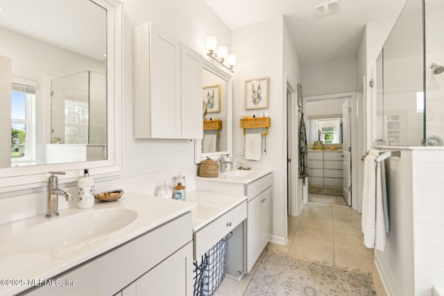 full bathroom with tile patterned floors, tiled shower, two vanities, and a sink