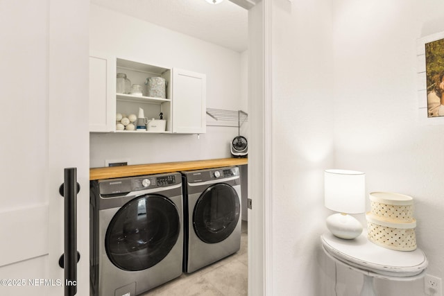 washroom with cabinet space, washing machine and dryer, and light tile patterned floors