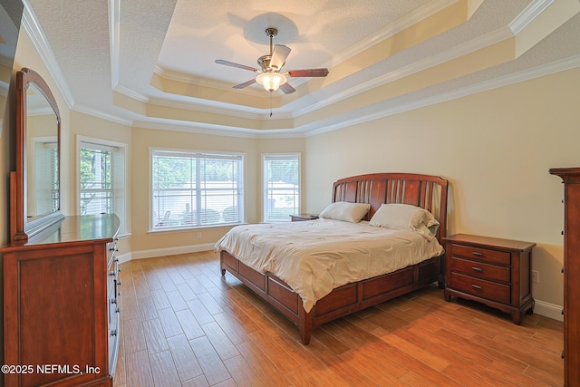 bedroom with a ceiling fan, crown molding, light wood-type flooring, a raised ceiling, and baseboards