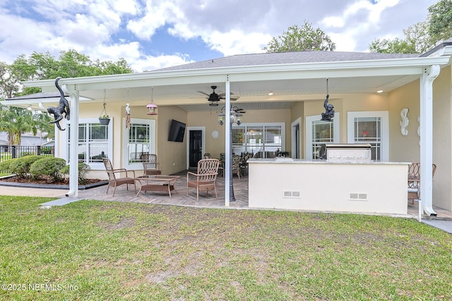 back of property with visible vents, an outdoor bar, a patio area, a lawn, and a ceiling fan