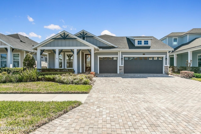 craftsman-style house with board and batten siding, a garage, decorative driveway, a shingled roof, and stone siding