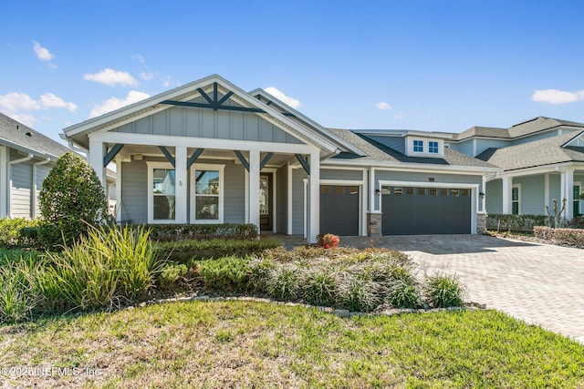view of front of property featuring a shingled roof, an attached garage, board and batten siding, decorative driveway, and covered porch