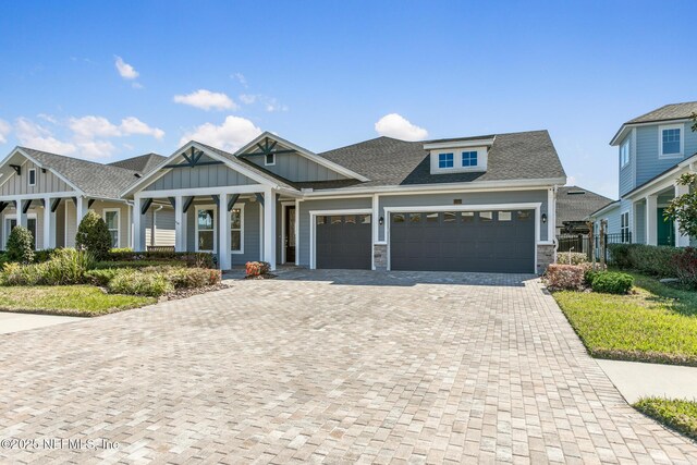 craftsman house featuring board and batten siding, covered porch, decorative driveway, an attached garage, and stone siding