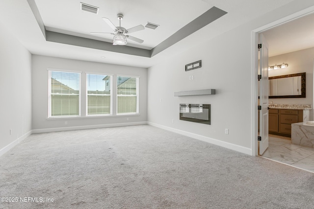 unfurnished living room featuring baseboards, ceiling fan, a raised ceiling, and visible vents