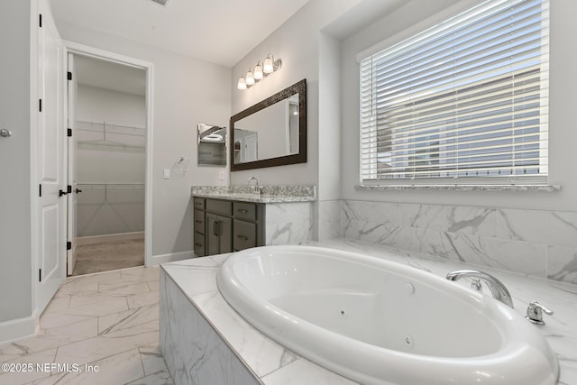 full bath featuring vanity, marble finish floor, a jetted tub, baseboards, and a walk in closet
