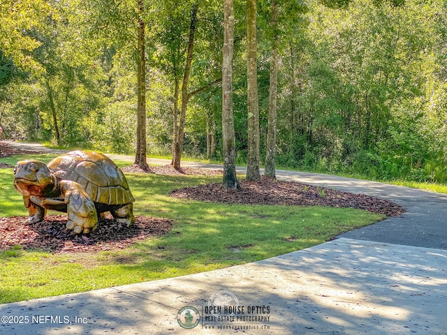 surrounding community with a lawn, driveway, and a wooded view