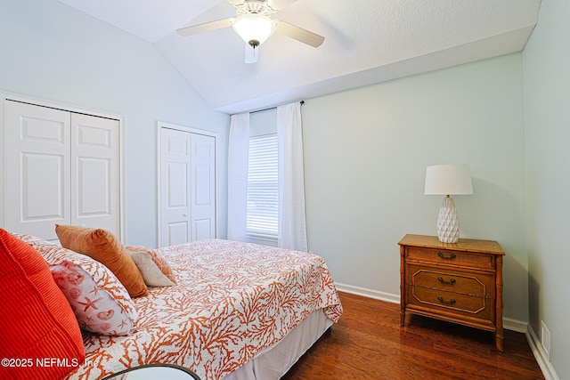 bedroom featuring two closets, visible vents, dark wood-style flooring, baseboards, and vaulted ceiling