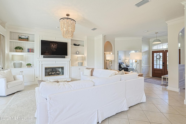 living room with visible vents, light tile patterned flooring, built in shelves, crown molding, and arched walkways