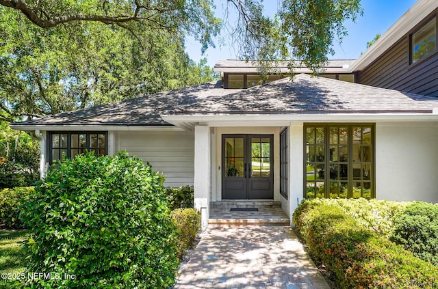 view of exterior entry featuring french doors and a shingled roof