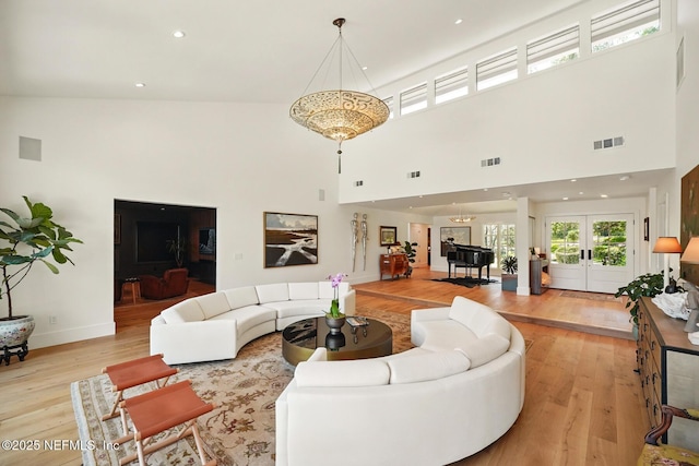 living room with light wood-style floors, baseboards, a towering ceiling, and visible vents