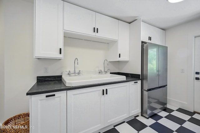 kitchen with freestanding refrigerator, dark countertops, light floors, white cabinetry, and a sink