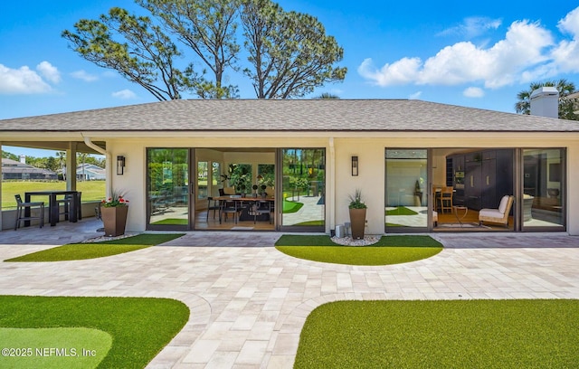 rear view of house with a shingled roof, stucco siding, and a patio area