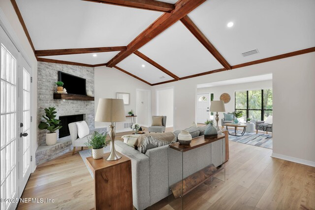 living room featuring visible vents, a fireplace, light wood-type flooring, baseboards, and vaulted ceiling with beams