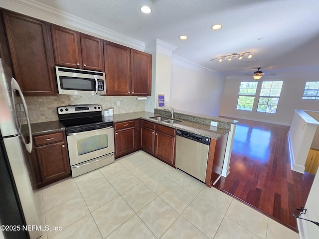 kitchen featuring appliances with stainless steel finishes, a sink, a peninsula, dark stone counters, and ornamental molding